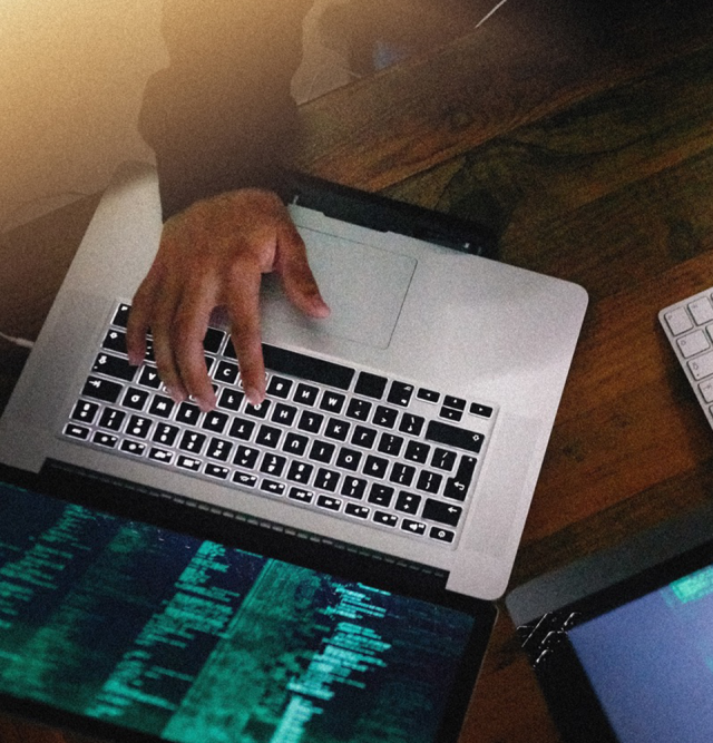 Hand typing on a laptop with a silver keypad, black keys, and a screen with neon green text